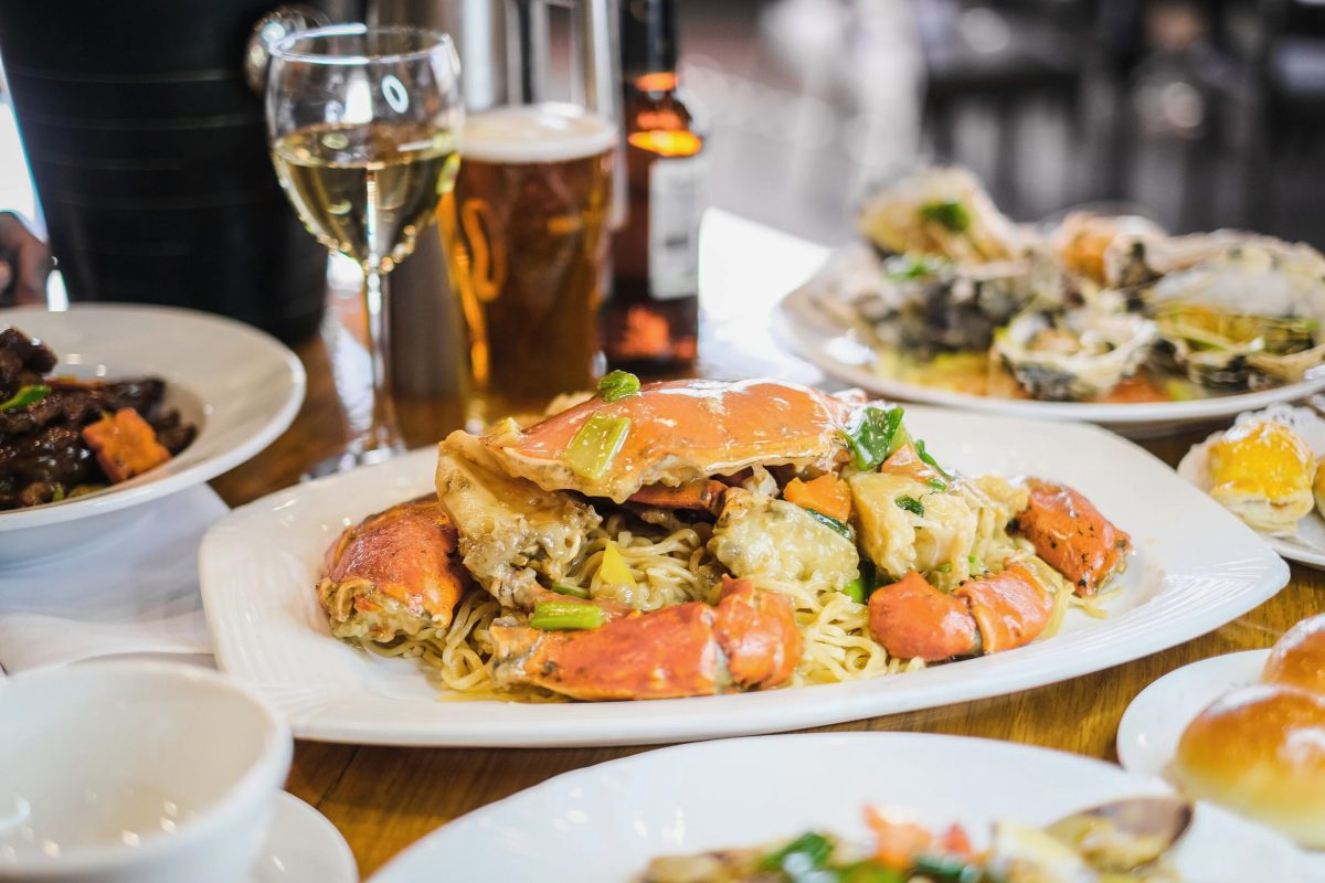 A whole crab served with noodle on a table with glasses of wine and beer and other dishes of Chinese food.