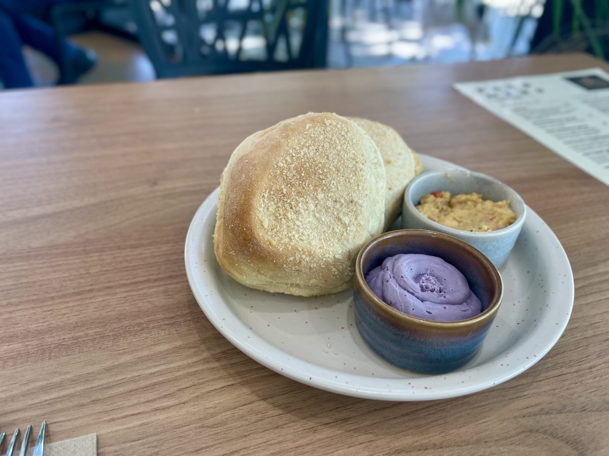 Two bread rolls with a crumb-topping on a plate with two ramekins. One is filled with purple ube cream cheese, the other with a spread made from roast capsicum and cheese. 