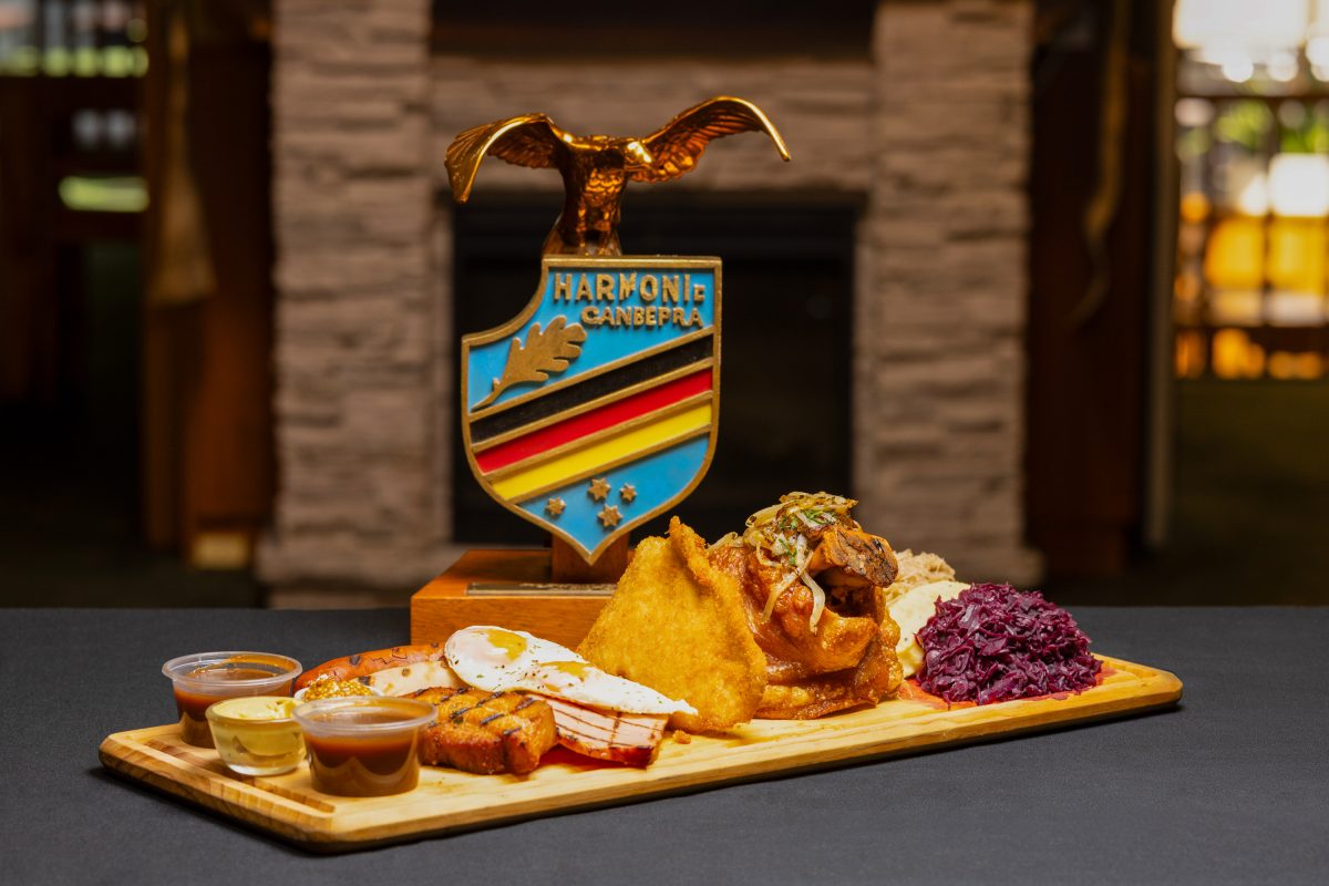A wooden platter with sausage, kraut, egg and bacon. The crest of the German club is displayed behind it.