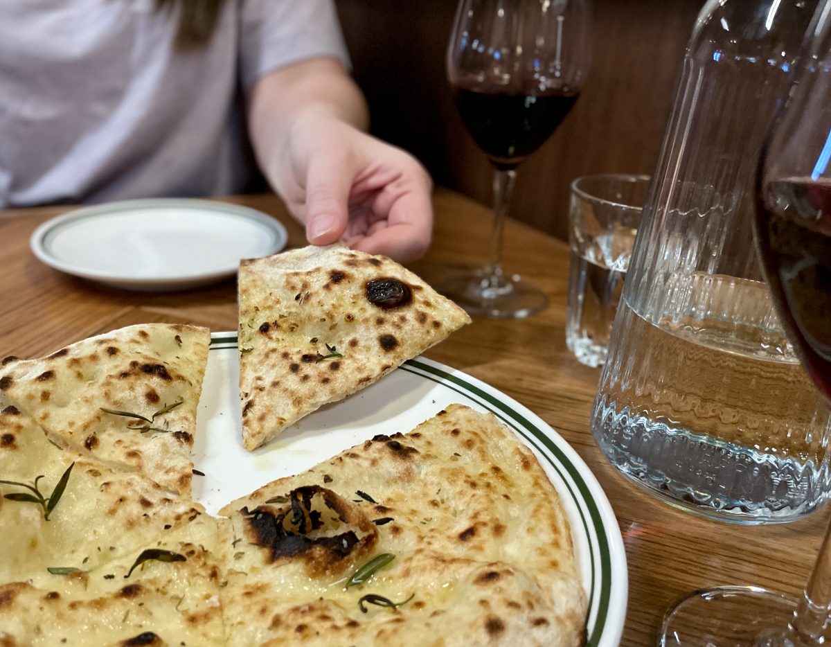 A hand picks up a piece of nicely charred flatbread with herbs.