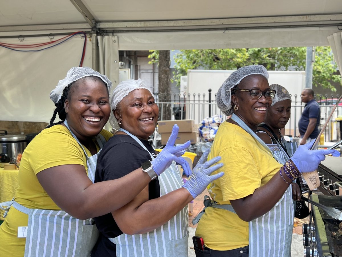 African women wearing aprons, hairnets and gloves smile and pose for the camera.