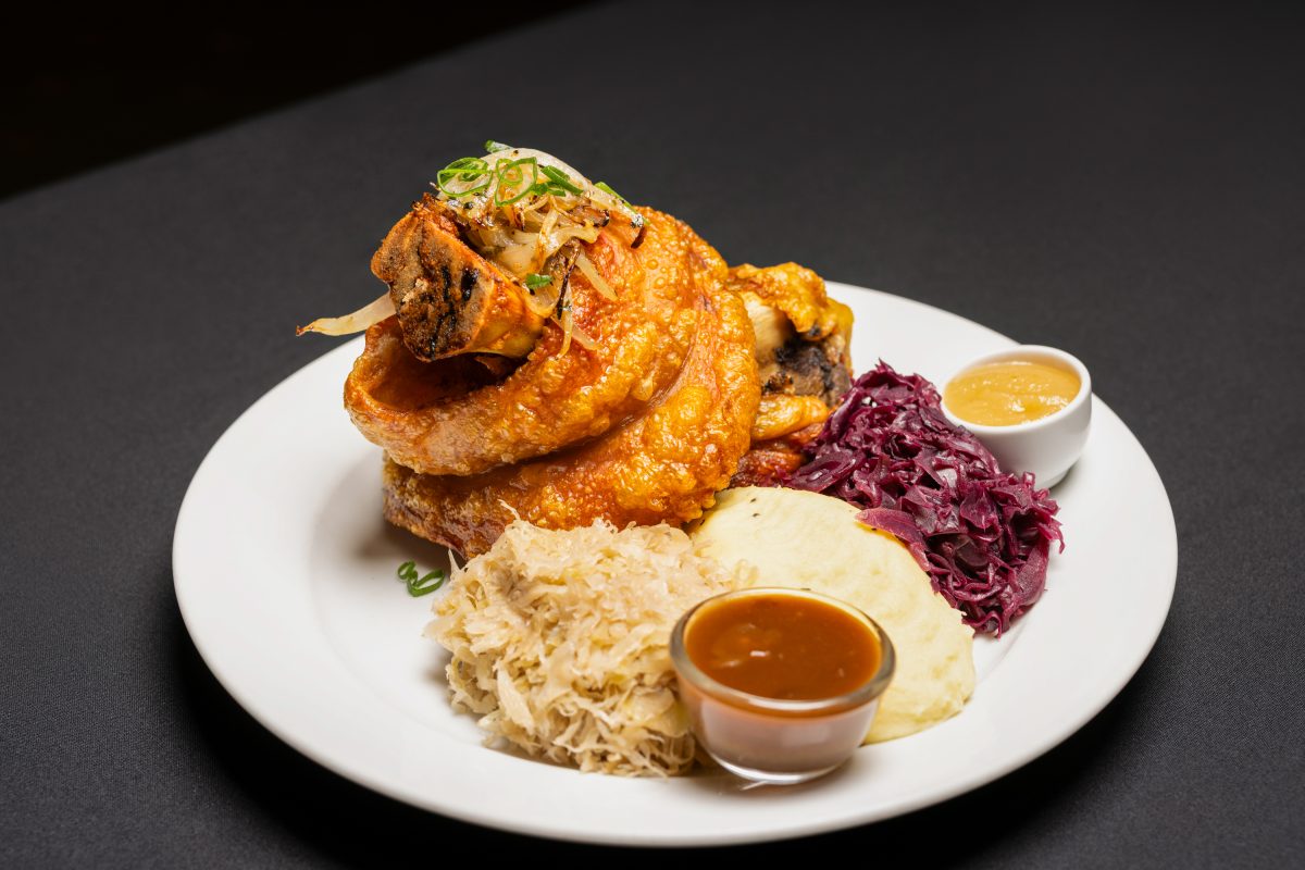 A white dinner plate with large pork knuckle including crispy crackling, potato mash, sauerkraut and gravy.