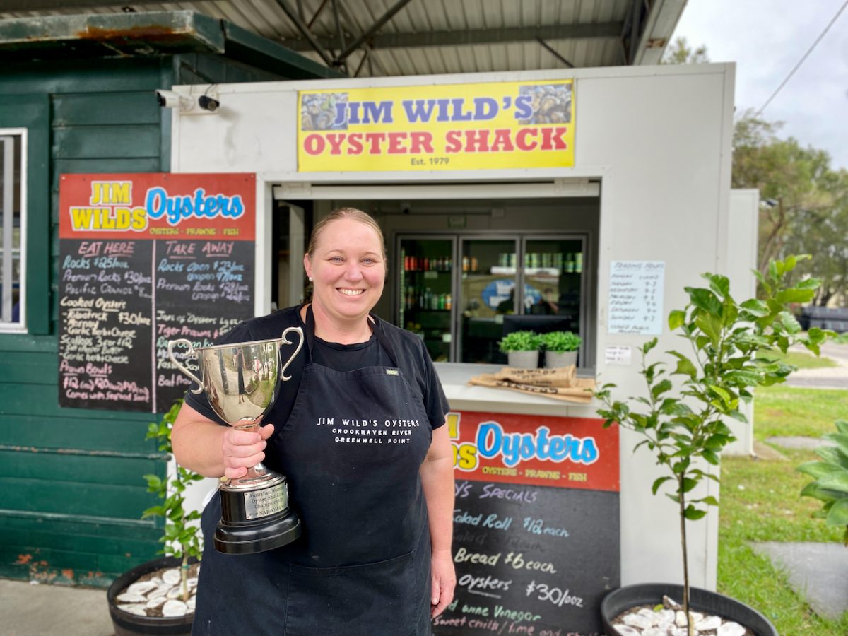 Sally holds a trophy and smiles in front of the Jim Wild's Oyster Shack counter