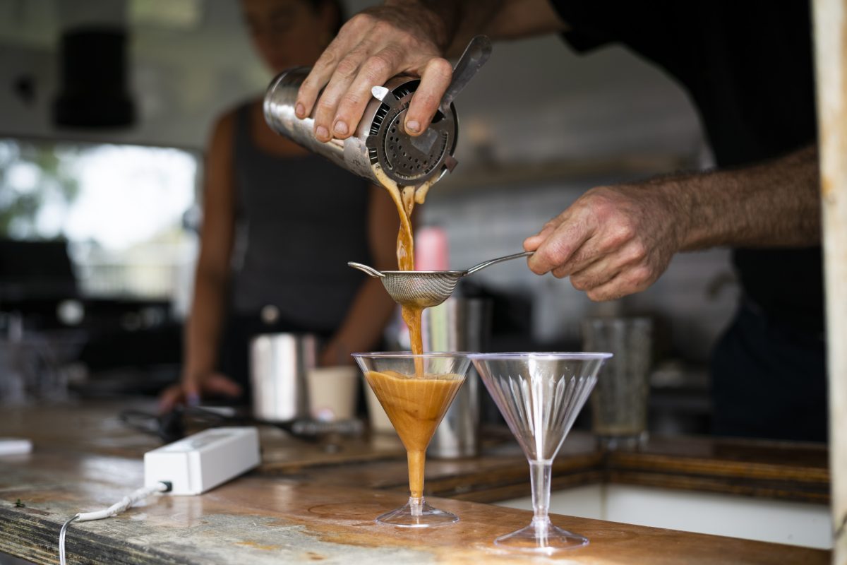 A close-up of a man pouring drinks with a cocktail shaker