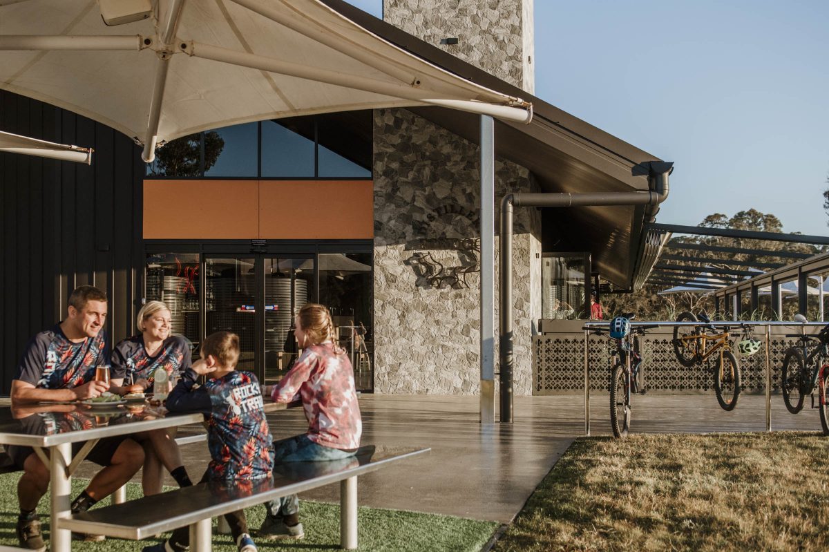 Exterior of distillery with people sitting at a dining table in cycling clothes and bicycles nearby